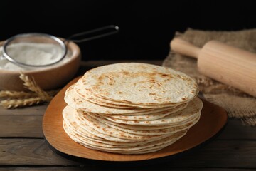 Many tasty homemade tortillas and rolling pin on wooden table
