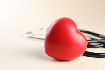 Stethoscope and red heart on beige background, closeup. Space for text