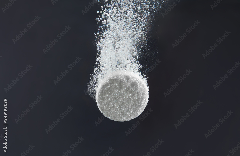 Sticker Effervescent pill dissolving in water on dark background, closeup