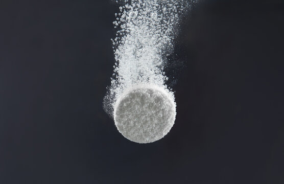 Effervescent pill dissolving in water on dark background, closeup