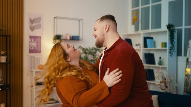 Romantic plus size couple dancing in room, enjoying date, smiling and talking