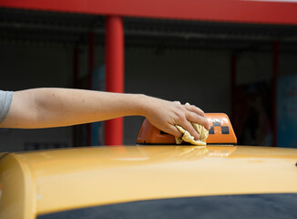 A close-up of a hand wiping a yellow cloth across the top of a taxis light. The taxi is yellow and...