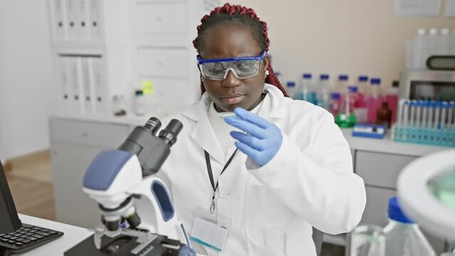 African woman scientist analyzing samples with microscope in biomedical research lab