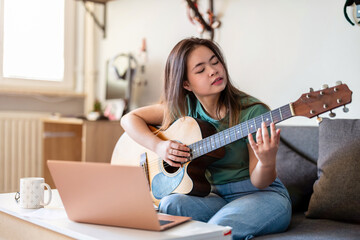 Young woman playing guitar at home
