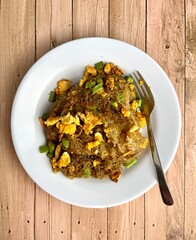 Stir fried sweet soy sauced rice noodle vermicelli with scrambled eggs and long beans in plate from above top view angle isolated food photography on vertical wooden background. Bihun goreng telur.