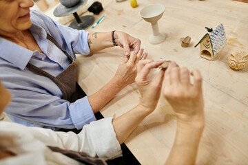 A mature lesbian couple works on pottery in a cozy art studio.