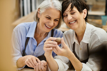 Two women in a pottery studio, laughing and looking at a clay creation.