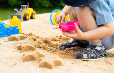 A child makes sand figures in a sandbox. Child in the fresh air. Play in the sandbox