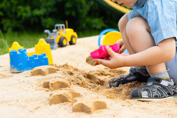 A child makes sand figures in a sandbox. Child in the fresh air. Play in the sandbox