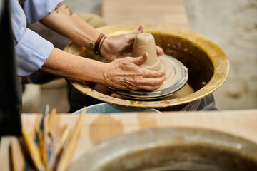 A close-up of a mature woman working on a pottery wheel in an art studio.