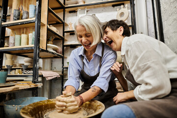 A lesbian couple enjoys pottery class, laughing as one shapes clay on a wheel.