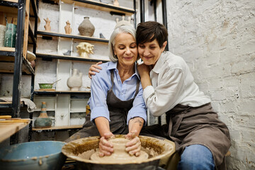 Two mature women, a lesbian couple, are working on pottery in a cozy art studio.