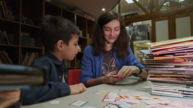 Speech therapist working with boy on pronunciation skills. Teacher shows the cards, guiding the child through learning foreign languages, supportive educational environment