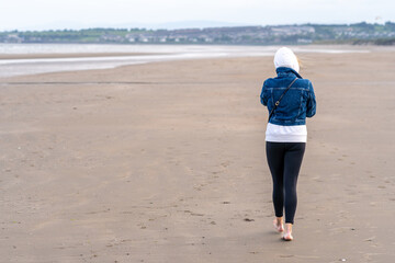 Sporty woman with bare feet on the sandy beach during windy day. Back view