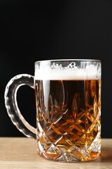 Mug with fresh beer on wooden table against black background, closeup