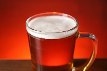 Mug with fresh beer on table against red background, closeup