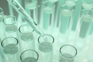 Dripping liquid from pipette into test tube on light green background, closeup