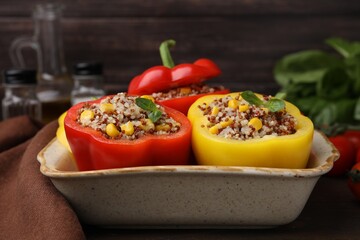 Quinoa stuffed bell peppers and basil in baking dish on table, closeup