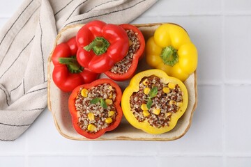Quinoa stuffed bell peppers and basil in baking dish on white tiled table, top view