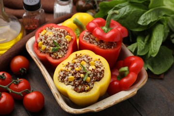 Quinoa stuffed bell peppers in baking dish, basil and tomatoes on wooden table, closeup