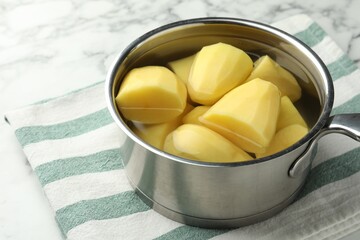 Raw potatoes in saucepan on white marble table