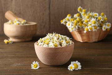 Dry and fresh chamomile flowers in bowl on wooden table