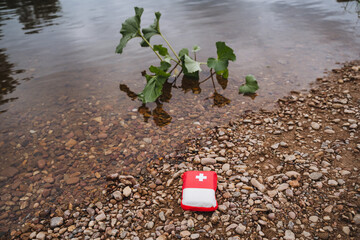 First Aid Kit by a riverside with green plants in calm water is essential for emergencies in a...