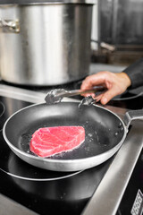 Close-up of a hand flipping a tuna steak in a frying pan, capturing the essence of cooking. Perfect for culinary themes