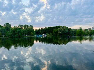 Fantastic cloudy sky reflection on the lake surface, trees silhouettes reflection on the lake, evening twilights lake in the park