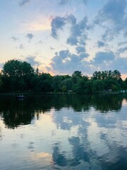 Fantastic cloudy sky reflection on the lake surface, trees silhouettes reflection on the lake, evening twilights lake in the park