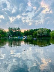 Fantastic cloudy sky reflection on the lake surface, trees silhouettes reflection on the lake, evening twilights lake in the park