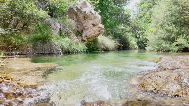 A river with a rock in the middle. The water is clear and calm