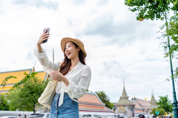 Fototapeta premium Joyful Asian Woman Taking Selfie at Famous Thai Landmark
