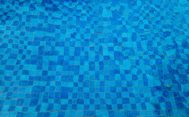 Top view space of clear water surface is rippling on swimming pool, blue grid mosaic tiles background. Empty space at poolside on sunny day, summer background poster concept.