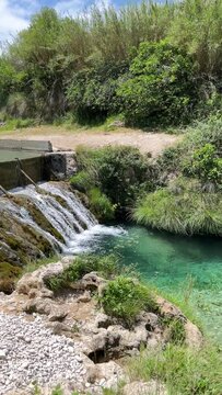 A waterfall is flowing into a river. The water is clear and the rocks are covered in moss. The scene is peaceful and serene