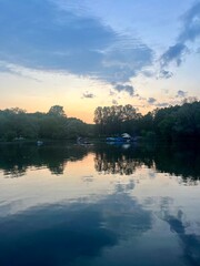Fototapeta premium Fantastic cloudy sky reflection on the lake surface, trees silhouettes reflection on the lake, evening twilights lake in the park