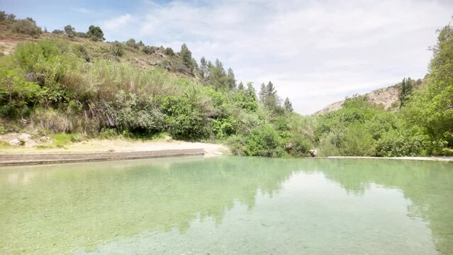 A beautiful lake with a green hill in the background. The water is clear and calm. The scene is peaceful and serene