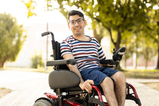 A person with a disability sits in a wheelchair at an outdoor park at sunset.The adult man is smiling at the camera happily.Disabled people in wheelchairs concept.