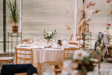 Valmiera, Latvia - September 9, 2023 -  A beautifully set wedding reception table with floral centerpiece, elegant tableware, and decorative elements in a bright, airy venue.