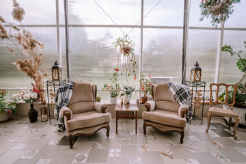 Valmiera, Latvia - September 9, 2023 - Cozy sitting area with two vintage armchairs, plants, and decorative items in a sunlit room with large windows, creating a comfortable and inviting atmosphere.