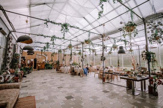 Valmiera, Latvia - September 9, 2023 - Elegant event hall with tables set for a celebration, decorated with hanging plants, flowers, and chandeliers, creating a sophisticated ambiance.