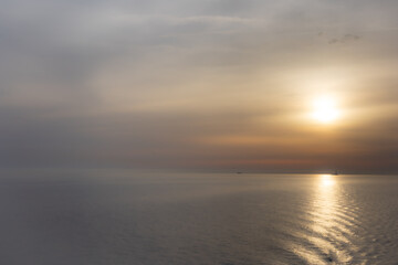 Golden sunset over the Mediterranean Sea with a ship and lighthouse on the horizon.