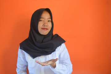 A friendly and successful Asian Muslim woman wearing a batik shirt with an orange background exclaimed excitedly while raising her two index fingers upwards, showing something.