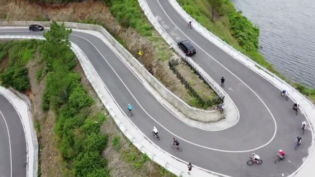 A winding road in Sibea-bea, on the shores of Lake Toba Samosir, North Sumatra, Indonesia. Cyclists pass by. Taken from above using a drone camera.