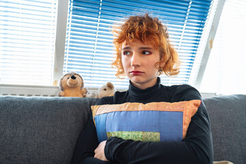 portrait naked crying teenage girl, with red curly hair, sitting on sofa, hugging pillow, in fetal...