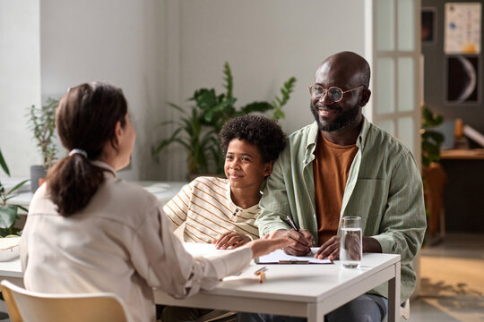 Portrait of happy African American father and son consulting with lawyer in office and signing documents