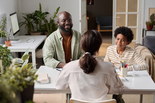 Back view of young woman speaking to smiling African American family of father and son in consultation over table