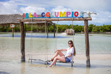 happy tourist blondie woman with long hair on a swing in the water of the tropical bay in sea shore