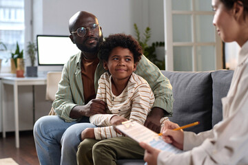 Portrait of smiling father and son listening to social worker in consultation on family...