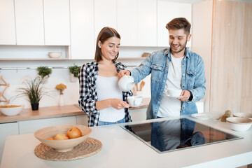 young happy man and woman in kitchen, breakfast, couple together in morning, smiling, having tea